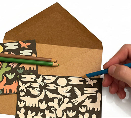 Hand holding a pen with two greeting cards featuring animal patterns and a brown envelope on a white background.