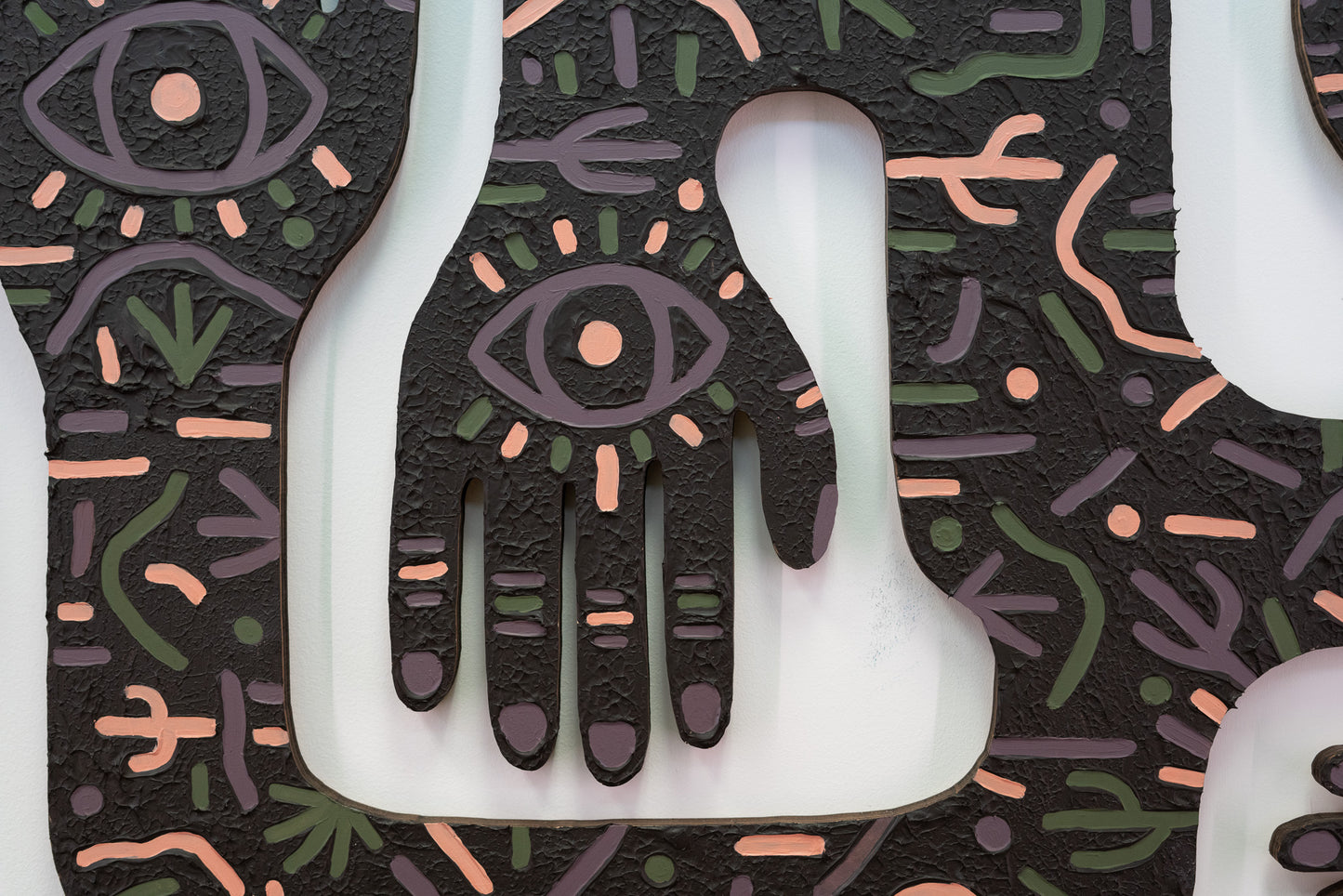 A close up of a laser cut  art work. The art work has high texture and eyes on the hands